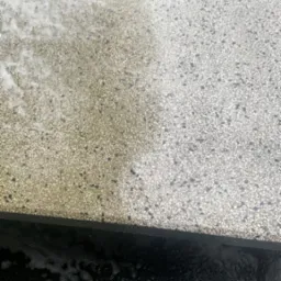 Fragment kostki brukowej, widoczna różnica między czystą, jasną częścią po lewej stronie a brudną, ciemniejszą częścią po prawej, w dolnej części woda z pianą.