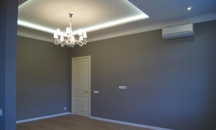 Wnętrze pokoju po remoncie: szare ściany, białe listwy przypodłogowe i sufitowe z oświetleniem LED, parkiet na podłodze, białe drzwi, klimatyzator na ścianie, żyrandol. Widoczne gniazdka...