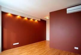 Pusty pokój z brązowymi ścianami, drewnianą podłogą i klimatyzatorem. Oświetlenie punktowe w suficie i listwa przypodłogowa.