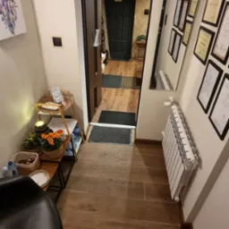 Wnętrze salonu z drewnianą podłogą, widok na otwarte drzwi do gabinetu z czarnymi elementami, dekoracje na ścianie, w tym lustro z certyfikatami i obraz z łapaczem snów.