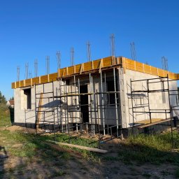 BALEN Inżynieria Budowlana Dawid Balicki - Surowy stan domu z betonu komórkowego, z widocznymi rusztowaniami i zbrojeniami, w otoczeniu zieleni i błękitnego nieba, w trakcie budowy.