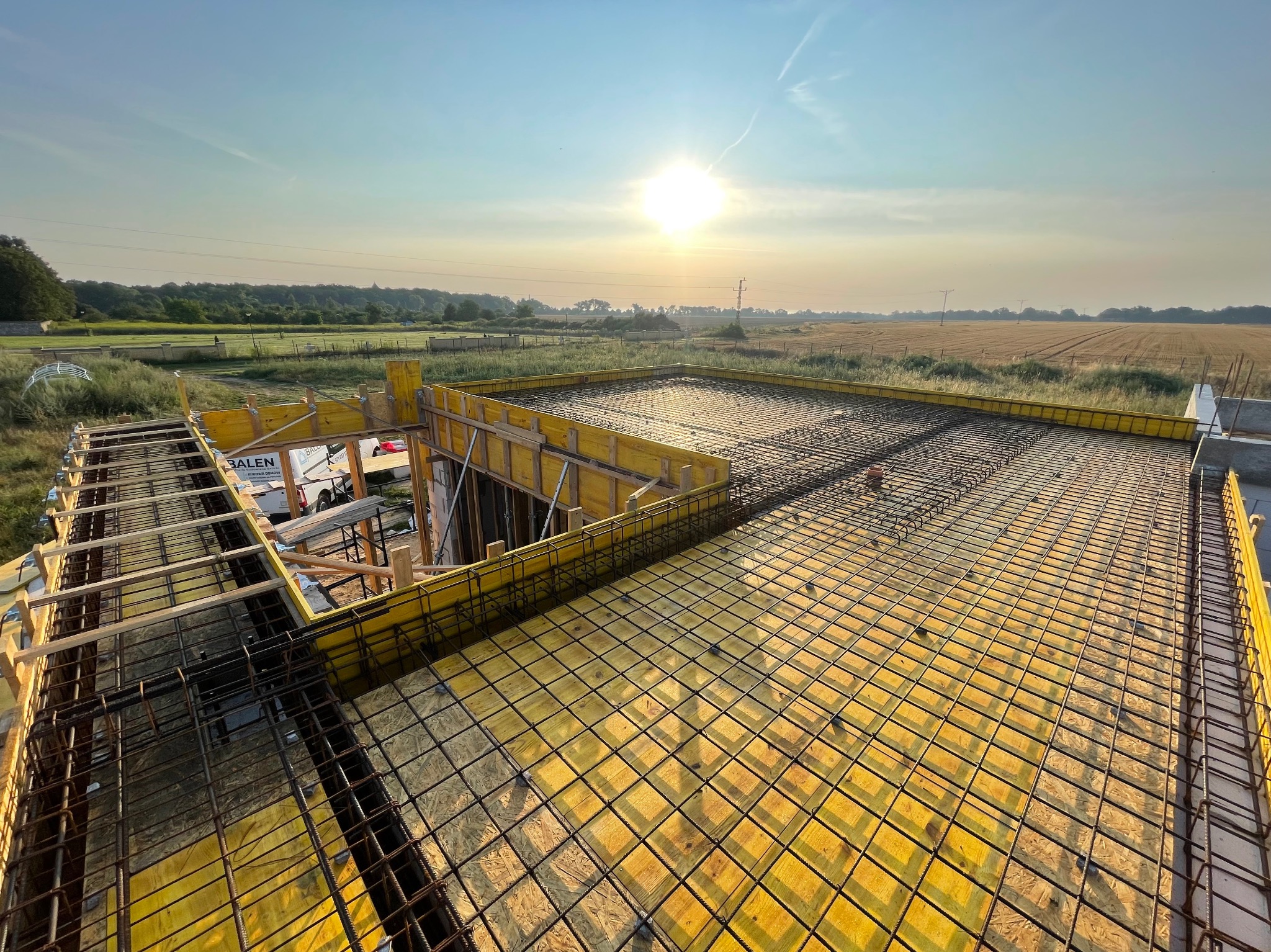 Zbrojenie stropu w deskowaniu z widokiem na pola uprawne w tle, wczesnym rankiem.