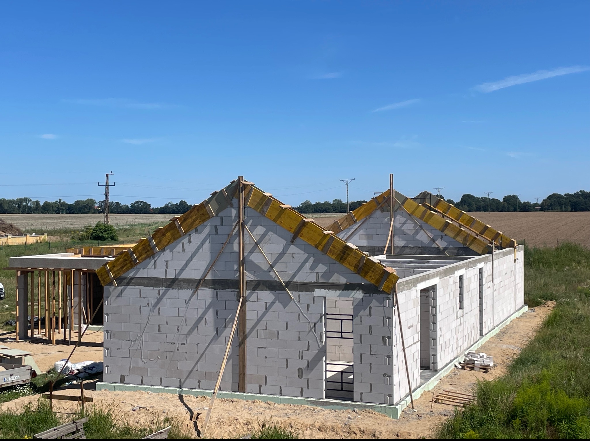 Wznoszenie ścian domu z betonu komórkowego; widoczne szalunki dachowe i fundamenty zabezpieczone izolacją przeciwwilgociową.