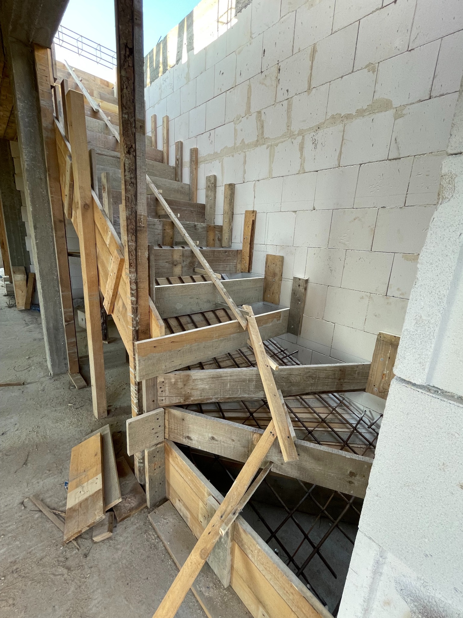 Konstrukcja drewniana szalunku schodów zbrojonych wewnątrz budynku. Ściany w tle wykonane z białych bloczków. Widoczny etap budowy.
