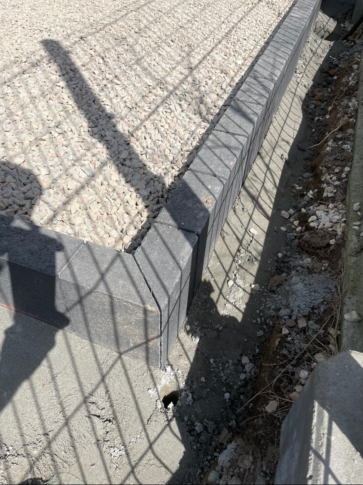 Szara kostka obrzeżowa oddzielająca żwir od ziemi, cień ogrodzenia, widok z góry, etap prac.