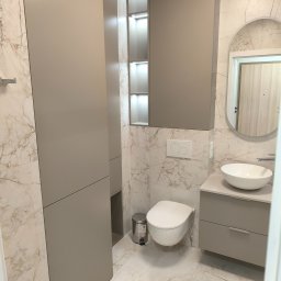 STOLMARK Marek Jakubczyk - Beżowa zabudowa łazienki z szafkami, toaletą i umywalką na blacie. Marmurowe płytki na ścianach i podłodze. Oświetlenie LED w szafkach.