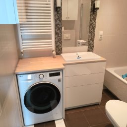 STOLMARK Marek Jakubczyk - Nowoczesna łazienka z pralką LG w zabudowie, blat z jasnego drewna, biała umywalka z szafką i grzejnik drabinkowy. Beżowe płytki, minimalistyczny design, funkcjonalne rozwiązanie.