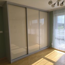 STOLMARK Marek Jakubczyk - Jasna szafa wnękowa z przesuwnymi drzwiami, wkomponowana w pokój z parkietem i oknem balkonowym, widziana w świetle dziennym.