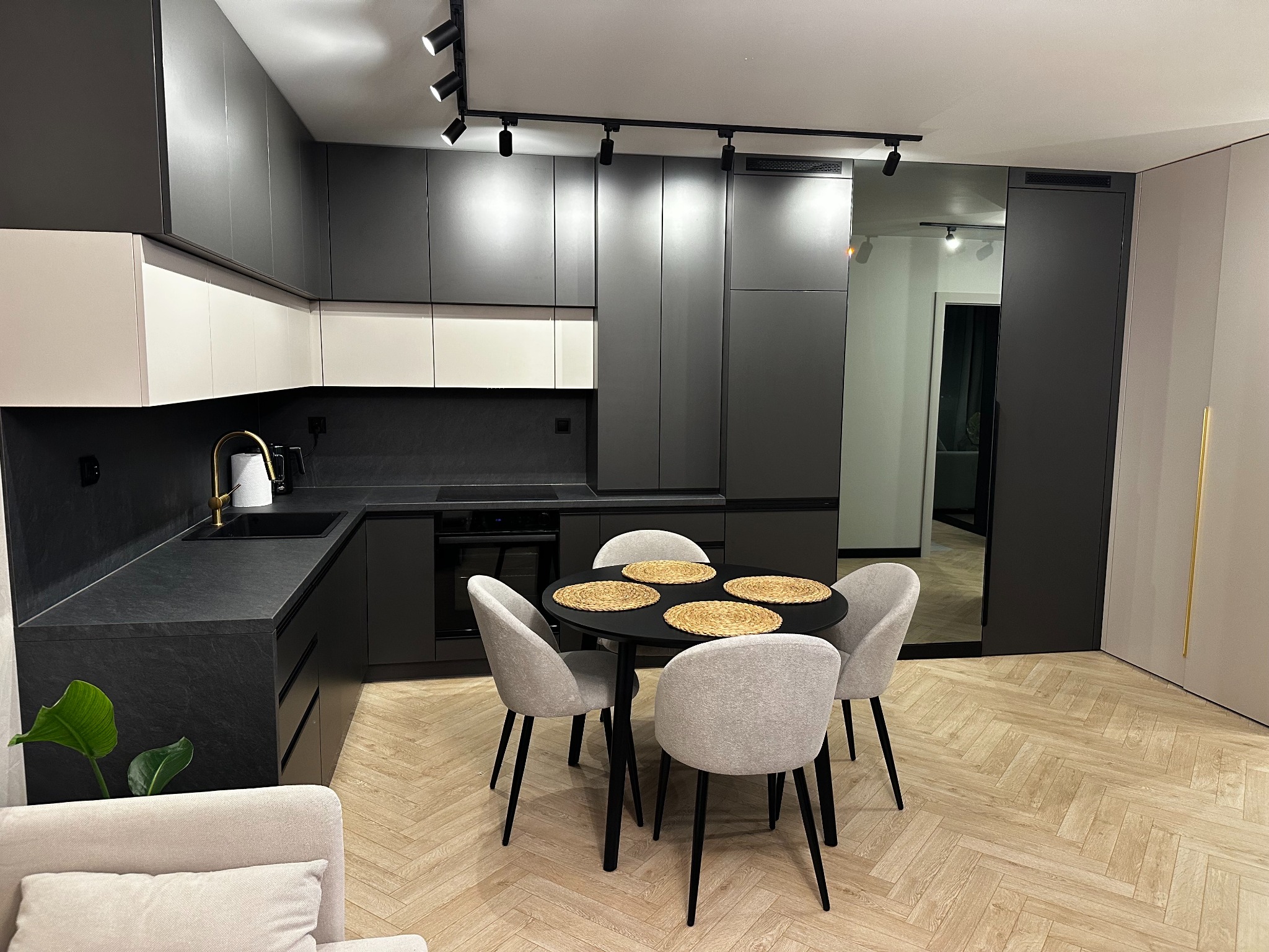 Nowoczesna kuchnia z czarnymi szafkami, białymi akcentami i okrągłym stołem jadalnym z czterema krzesłami na parkiecie ułożonym w jodełkę.