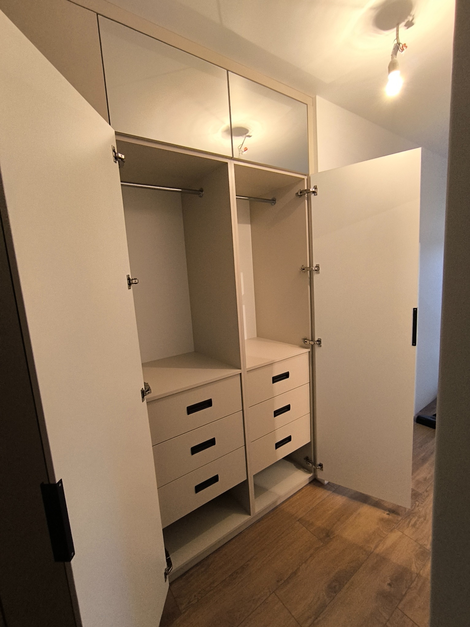 Jasna szafa wnękowa z szufladami i drążkami, otwarte drzwi ukazują wnętrze. Realizacja w Żegocinie. Minimalistyczny design, funkcjonalne rozwiązanie.