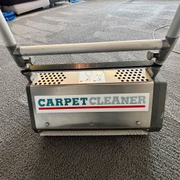 Pan do Plam Kompleksowo dla Czystości Artur Janiec - Profesjonalna maszyna do czyszczenia dywanów z napisem 'CARPET CLEANER' na tle szarego, wyczyszczonego dywanu.