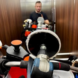 Pan do Plam Kompleksowo dla Czystości Artur Janiec - Polerka i inne narzędzia w windzie. Odbicie mężczyzny w lustrze windy. Przygotowanie do pracy, detale narzędzi i akcesoriów do czyszczenia.