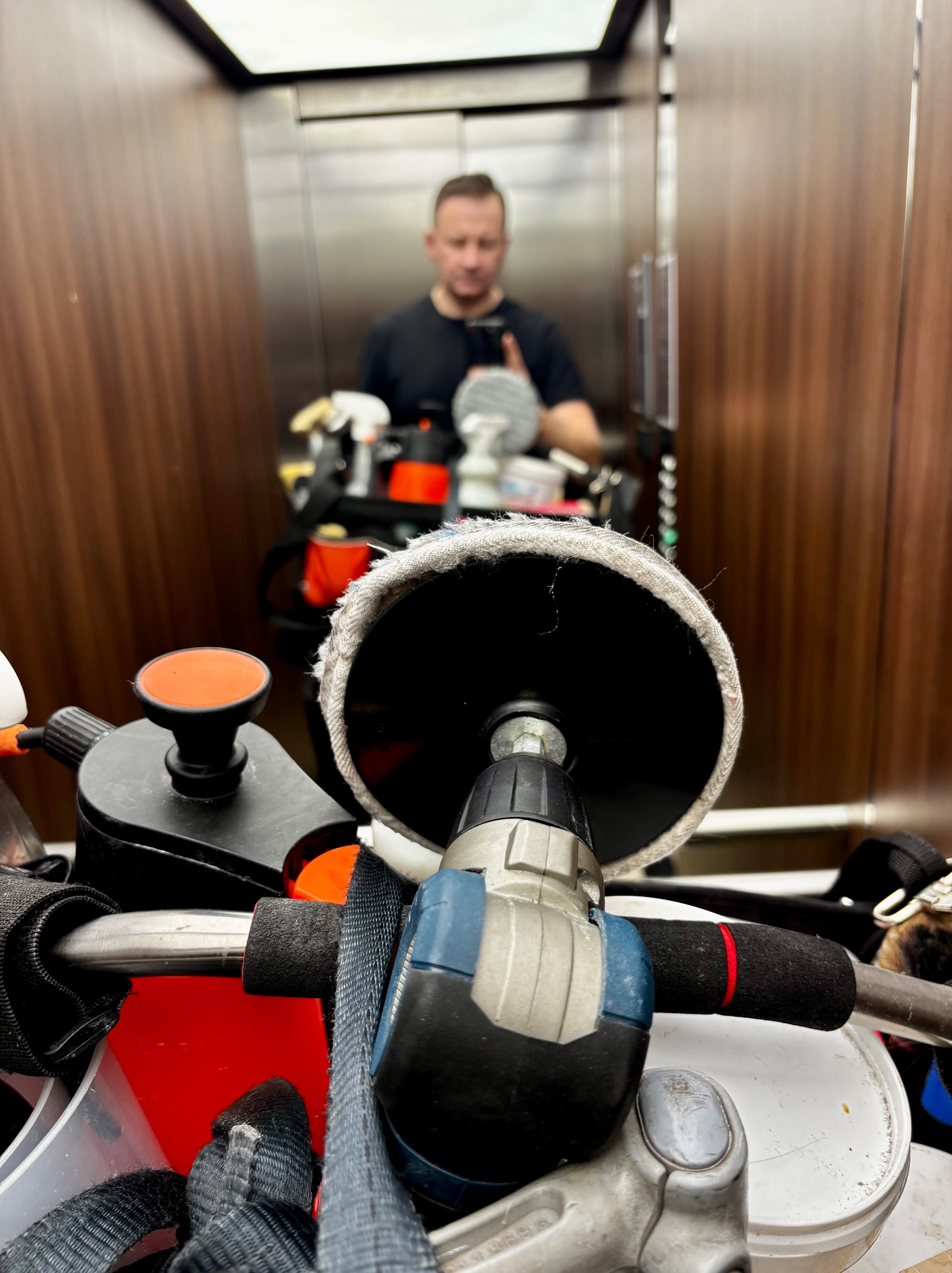 Polerka i inne narzędzia w windzie. Odbicie mężczyzny w lustrze windy. Przygotowanie do pracy, detale narzędzi i akcesoriów do czyszczenia.