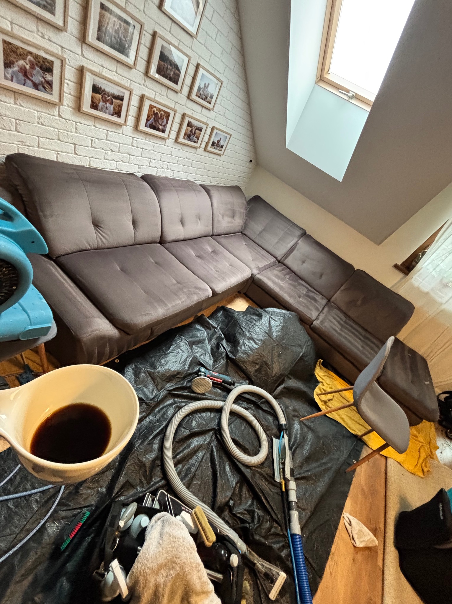 Narożnik z brązową tapicerką przygotowany do czyszczenia. Widoczne narzędzia, miska z brudną wodą i folia zabezpieczająca podłogę w pokoju na poddaszu.