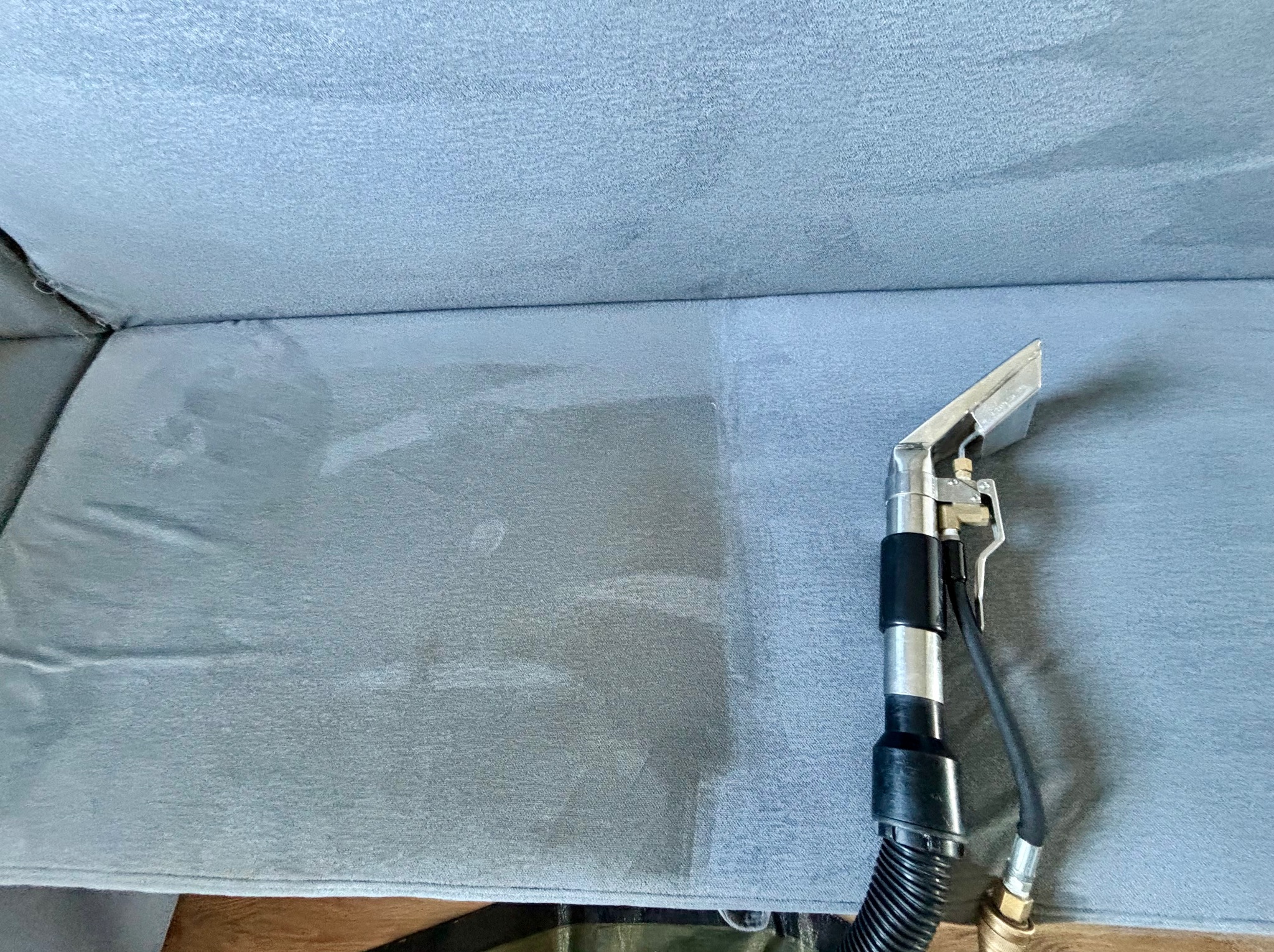 Szczegółowy widok fragmentu sofy w trakcie czyszczenia z użyciem profesjonalnego ekstraktora, ukazujący różnicę w odcieniu po zabiegu.