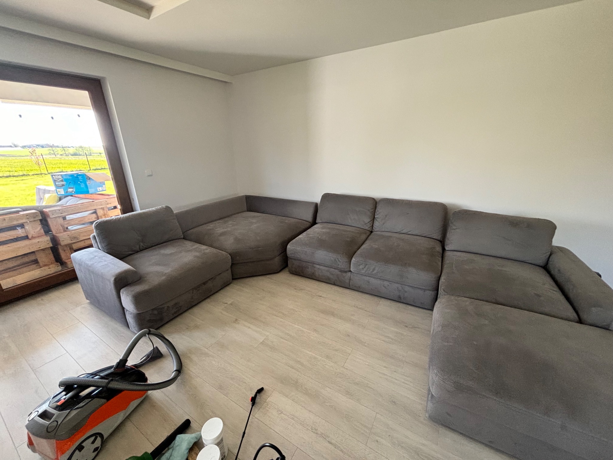 Szara modułowa sofa narożna w trakcie czyszczenia, widoczny odkurzacz piorący i akcesoria na jasnej podłodze.