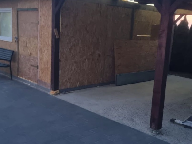 Surowy budynek gospodarczy z desek OSB, częściowo pod zadaszeniem, z widocznym fragmentem betonowej wylewki i szarej kostki brukowej.