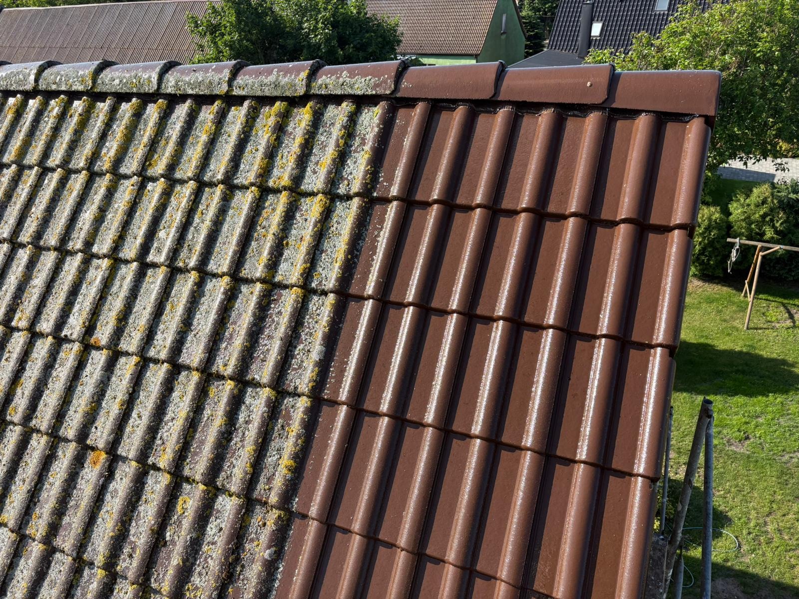 Częściowo wyczyszczony, brązowy dach z dachówki ceramicznej. Lewa strona pokryta mchem i porostami, prawa czysta. Widok z góry, w tle zieleń.
