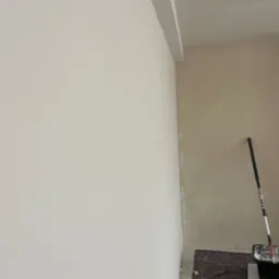 Świeżo pomalowana, jasna ściana z widocznym wałkiem malarskim i kuwetą, druga ściana w trakcie malowania, zabezpieczona podłoga.