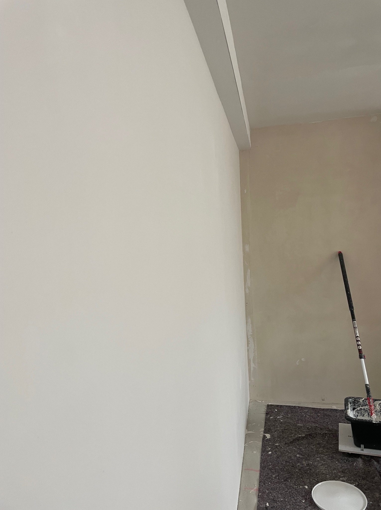 Świeżo pomalowana, jasna ściana z widocznym wałkiem malarskim i kuwetą, druga ściana w trakcie malowania, zabezpieczona podłoga.