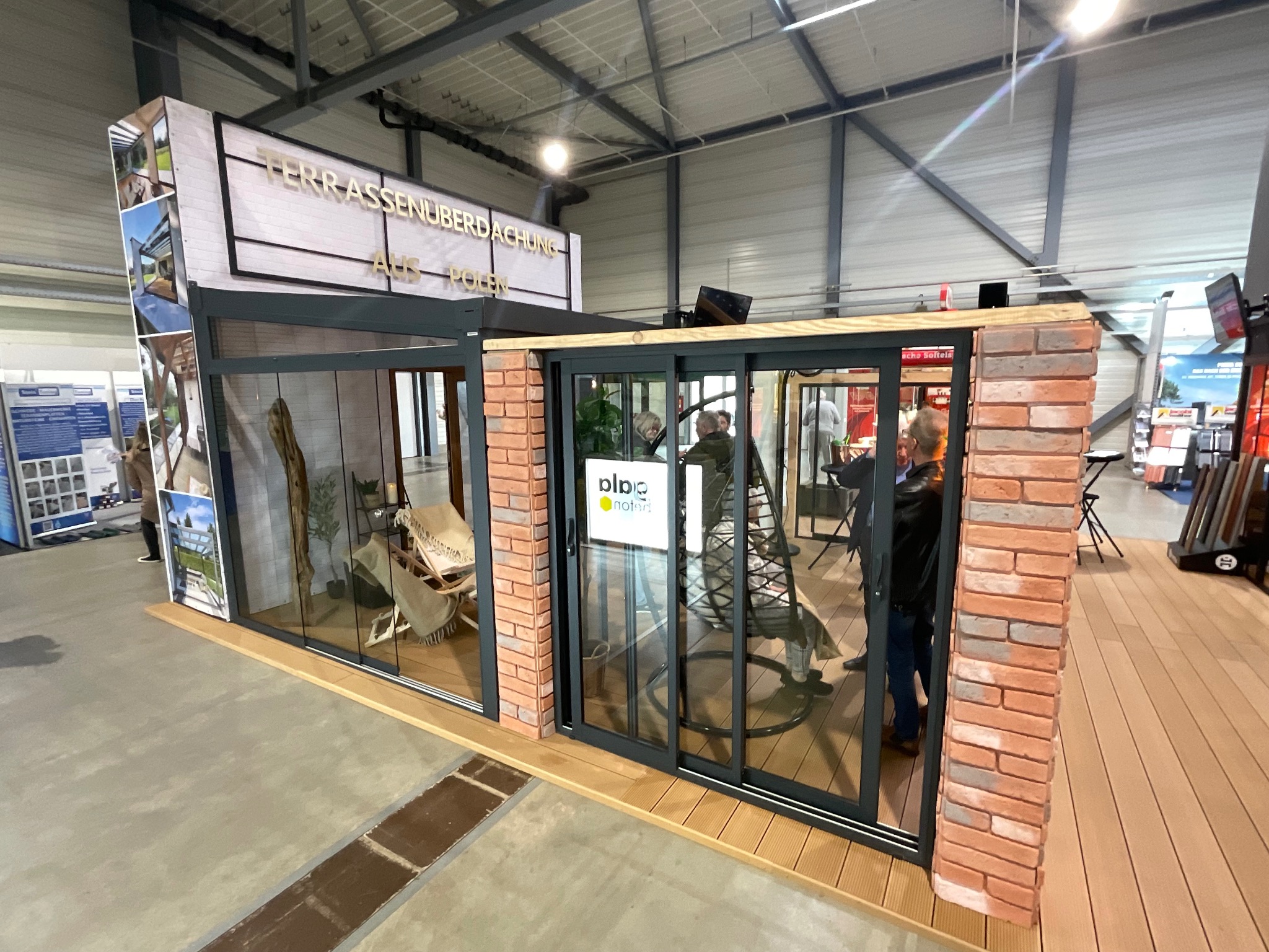 Ekspozycja zadaszenia tarasu z przesuwnymi szklanymi drzwiami, wykończona cegłą i drewnem, prezentowana na targach.