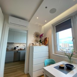 Loxmax Energy Solutions - Nowoczesne wnętrze mieszkania w Koronowie z klimatyzacją, widok na kuchnię z drewnianą podłogą, białą komodę z dekoracjami i stolik z owocami przy oknie.