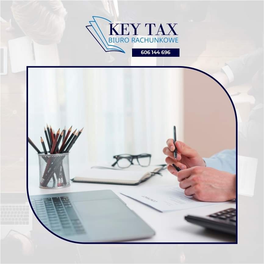 Biuro rachunkowe Key Tax: dłoń trzymająca czarny długopis nad umową, laptop, kalkulator, ołówki w metalowym pojemniku i okulary na białym biurku w jasnym pomieszczeniu.