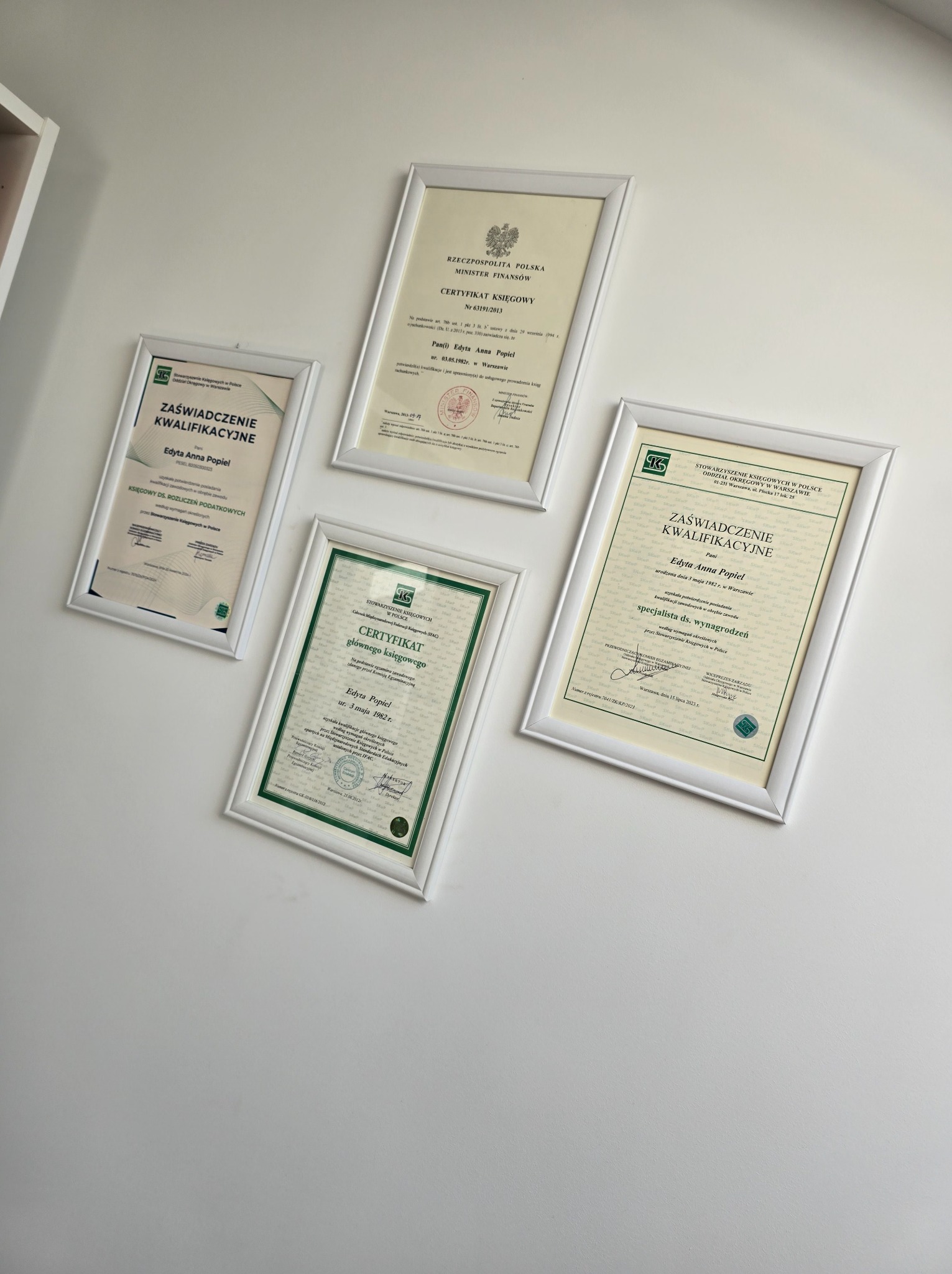 Ściana z czterema oprawionymi certyfikatami i zaświadczeniami kwalifikacyjnymi, w tym certyfikat księgowy Ministra Finansów oraz zaświadczenia Stowarzyszenia Księgowych w Polsce, wszystkie...
