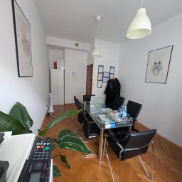 Kancelaria Radcy Prawnego Albert Białczyk - Sala konferencyjna z szklanym stołem, czarnymi krzesłami i laptopem. Na ścianie dyplomy i grafika. Podłoga z parkietu. W tle widoczny strój adwokacki.