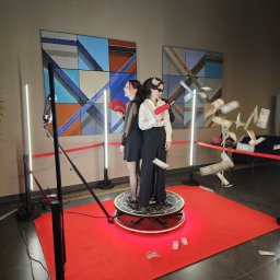 George Studio Kreatywne - Dwie kobiety pozują na obrotowej platformie fotobudki 360 stopni, w otoczeniu rekwizytów i rozrzuconych banknotów, przed abstrakcyjnym obrazem.