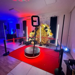 George Studio Kreatywne - Świetlna dekoracja imprezowa z obrotową platformą, czerwonym dywanem i balonami w kolorach złota i czerni. W tle DJ i efekty świetlne.