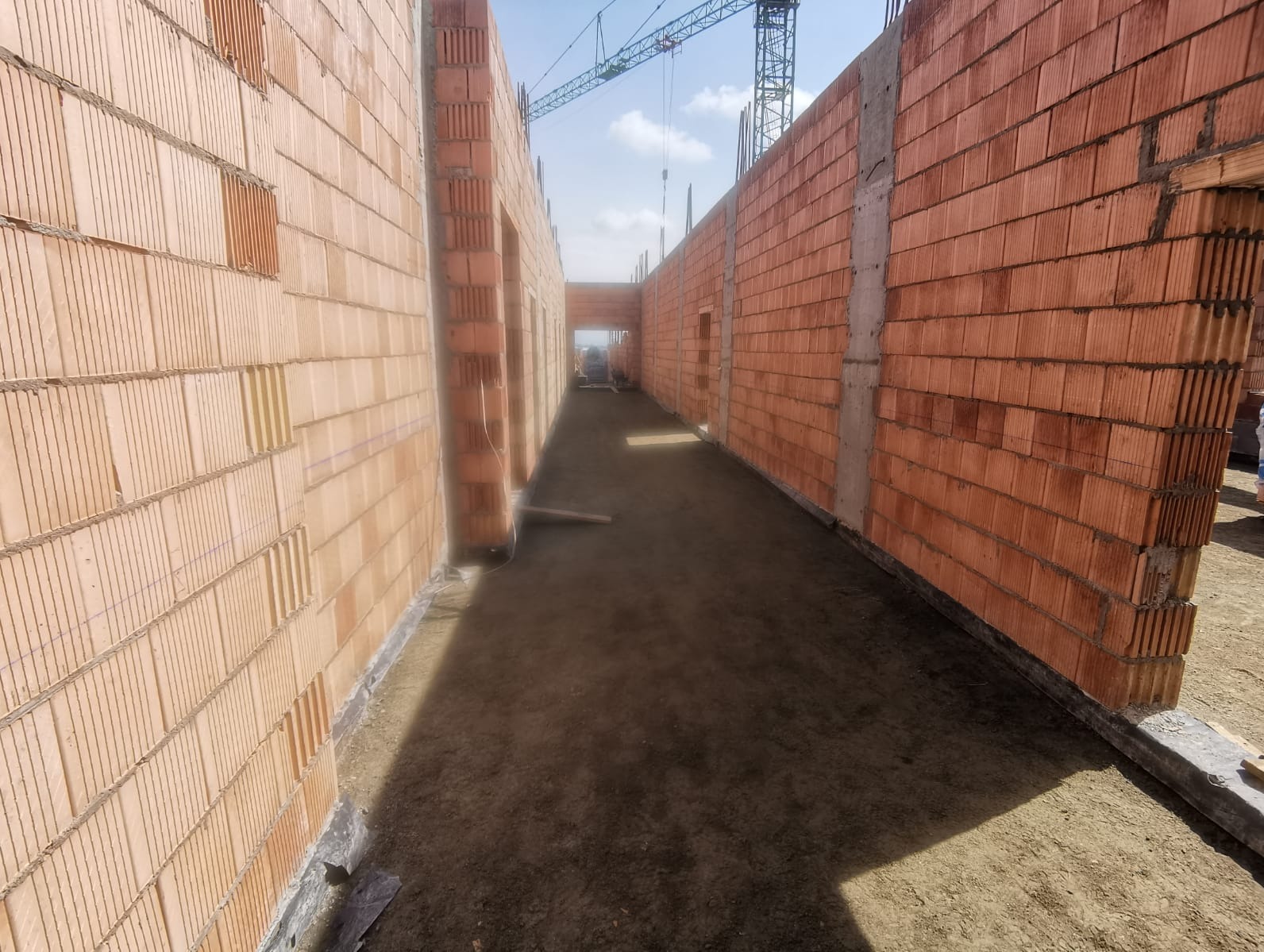 Wnętrze budynku w trakcie budowy z widocznymi ścianami z cegły ceramicznej, surowa podłoga i dźwig budowlany w tle.