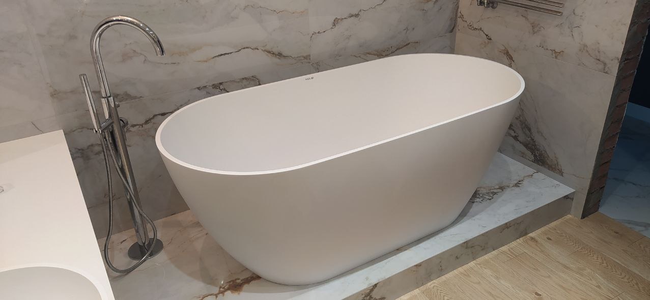 Wolnostojąca wanna w łazience z marmurowymi płytkami na ścianach i baterią podłogową.