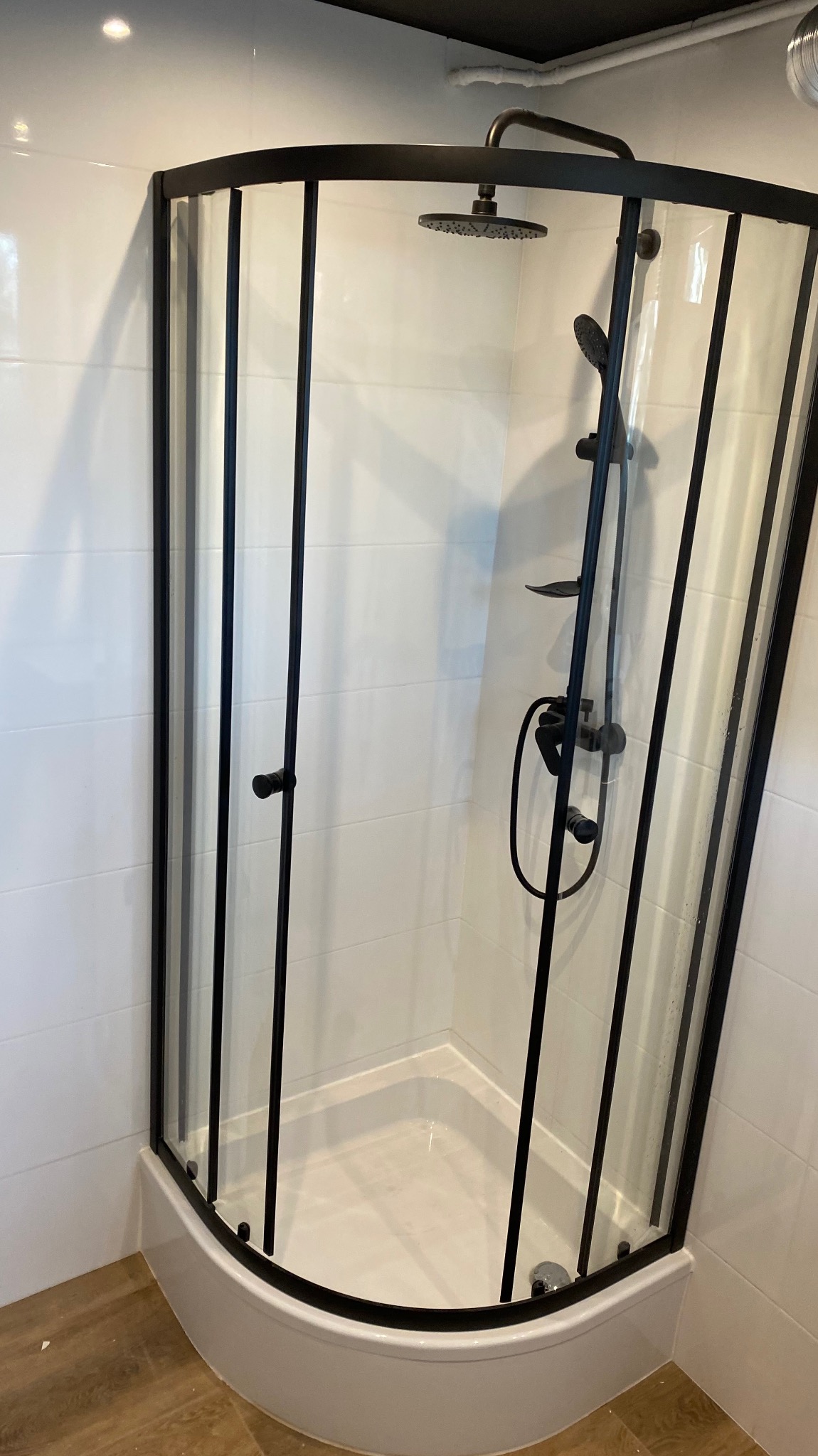 Nowoczesna kabina prysznicowa z czarnymi profilami i deszczownicą, białe płytki na ścianach, jasna podłoga. Minimalistyczny design łazienki po remoncie.