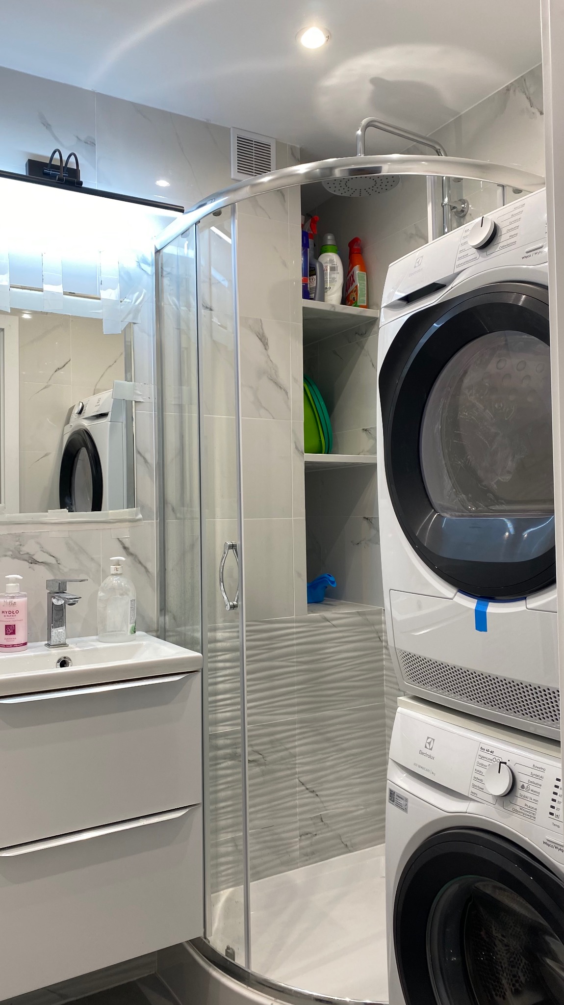 Nowoczesna łazienka po remoncie: kabina prysznicowa z marmurowymi płytkami, umywalka z szafką i pralka z suszarką Electrolux w zabudowie. Minimalistyczny design.