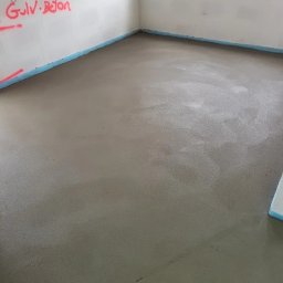Popów Podłogi & Posadzki - Świeżo wylana, gładka posadzka w pomieszczeniu w stanie surowym, zabezpieczona taśmą przy ścianach, z widocznym napisem 'Gulv Beton' na ścianie.