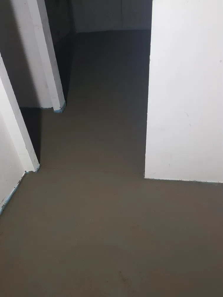 Świeżo wylana, gładka posadzka jastrychowa w pomieszczeniu z białymi filarami zabezpieczonymi niebieską taśmą, widok z góry.