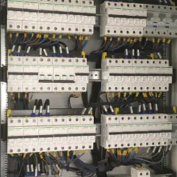 Rozdzielnica elektryczna z zainstalowanymi bezpiecznikami i okablowaniem, widoczne elementy marki Schneider Electric, ułożone w rzędach i kolumnach wewnątrz metalowej obudowy.