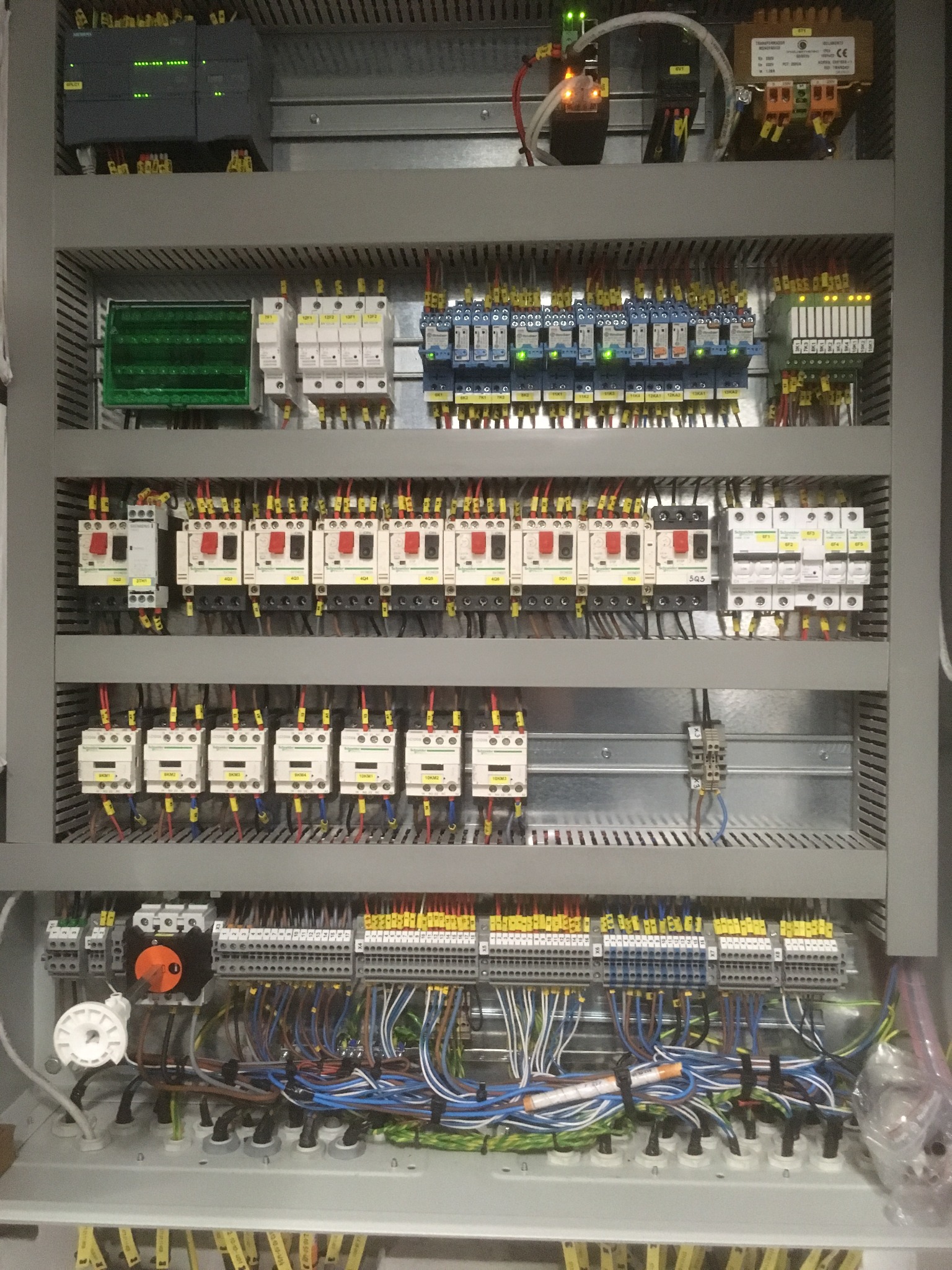 Rozbudowana szafa sterownicza z licznymi zabezpieczeniami, przekaźnikami i rozłącznikami, uporządkowane okablowanie w kolorowych izolacjach.