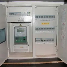 Otwarta szafka rozdzielcza z licznikiem energii elektrycznej i bezpiecznikami, widoczne klucze w zamku drzwi.