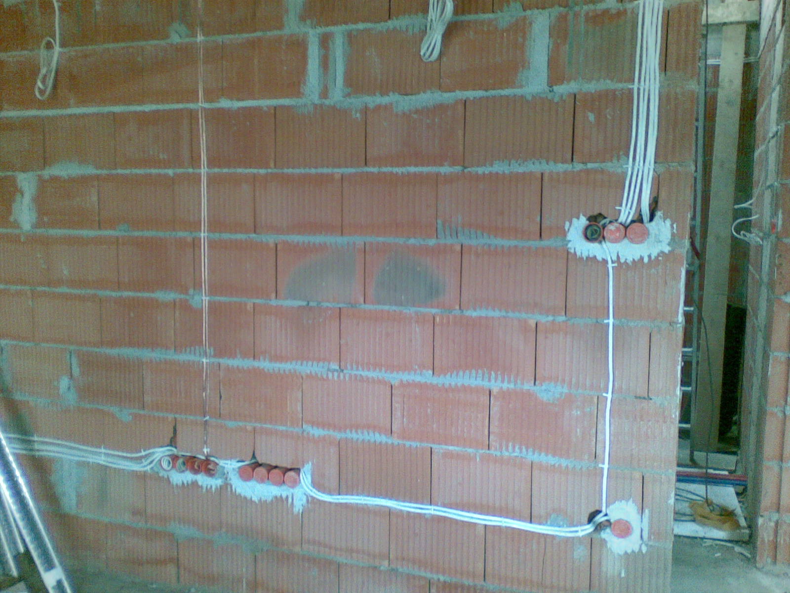 Instalacja elektryczna w trakcie montażu w nowym budynku z cegły, widoczne przewody i puszki elektryczne zamocowane w ścianie. Częściowo wykonane bruzdy pod kable.