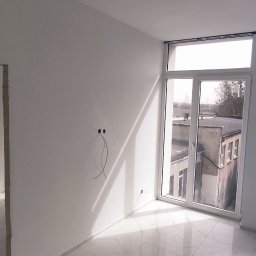 PERFEKT BUD SERHII HRYSHKO - Pomalowane na biało wnętrze z marmurową podłogą, widoczne wystające kable ze ściany i jasne światło wpadające przez okno.