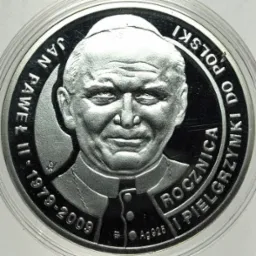 Srebrna moneta kolekcjonerska upamiętniająca Jana Pawła II, z wygrawerowanym wizerunkiem papieża i napisem 'Rocznica I Pielgrzymki Do Polski 1979-2009', umieszczona w przezroczystym etui.