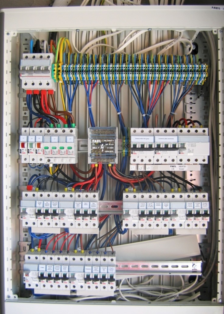 Rozdzielnica elektryczna z licznymi bezpiecznikami, przewodami o różnych kolorach i listwami zaciskowymi, zamontowana wewnątrz obudowy. Widoczny element zabezpieczający FAEL BR4-7.