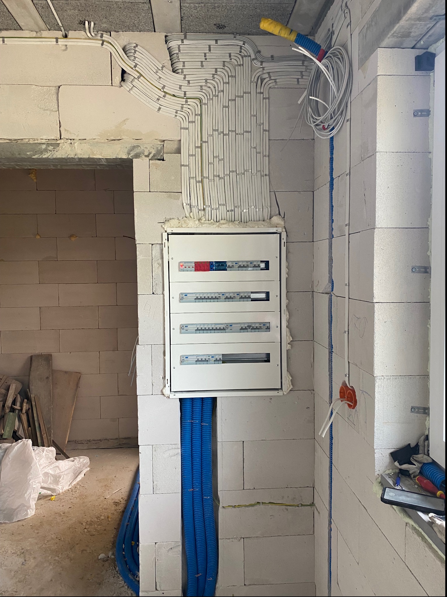 Rozdzielnica elektryczna zamontowana na ścianie z bloczków, z widocznymi przewodami ułożonymi w peszlach, instalacja w trakcie wykonywania.