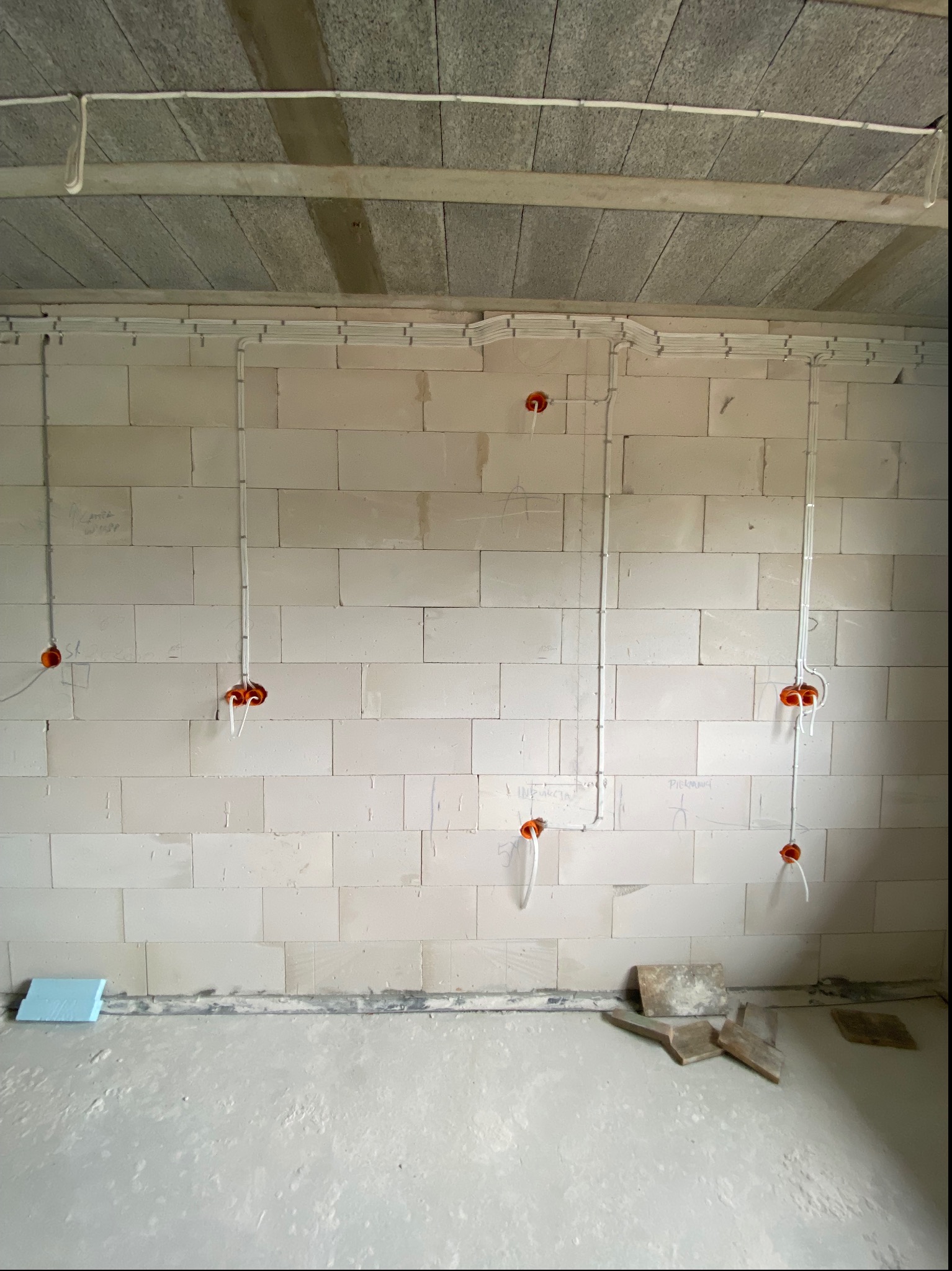 Rozprowadzenie instalacji elektrycznej w nowo budowanym domu z pustaków, widoczne kable w peszlach i puszki instalacyjne w ścianach oraz kable pod sufitem.