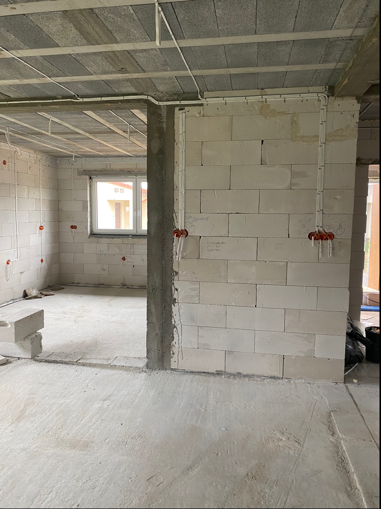 Surowy stan budynku z instalacją elektryczną: widoczne kable w peszlach, puszki elektryczne w ścianach z betonu komórkowego, okno w tle.