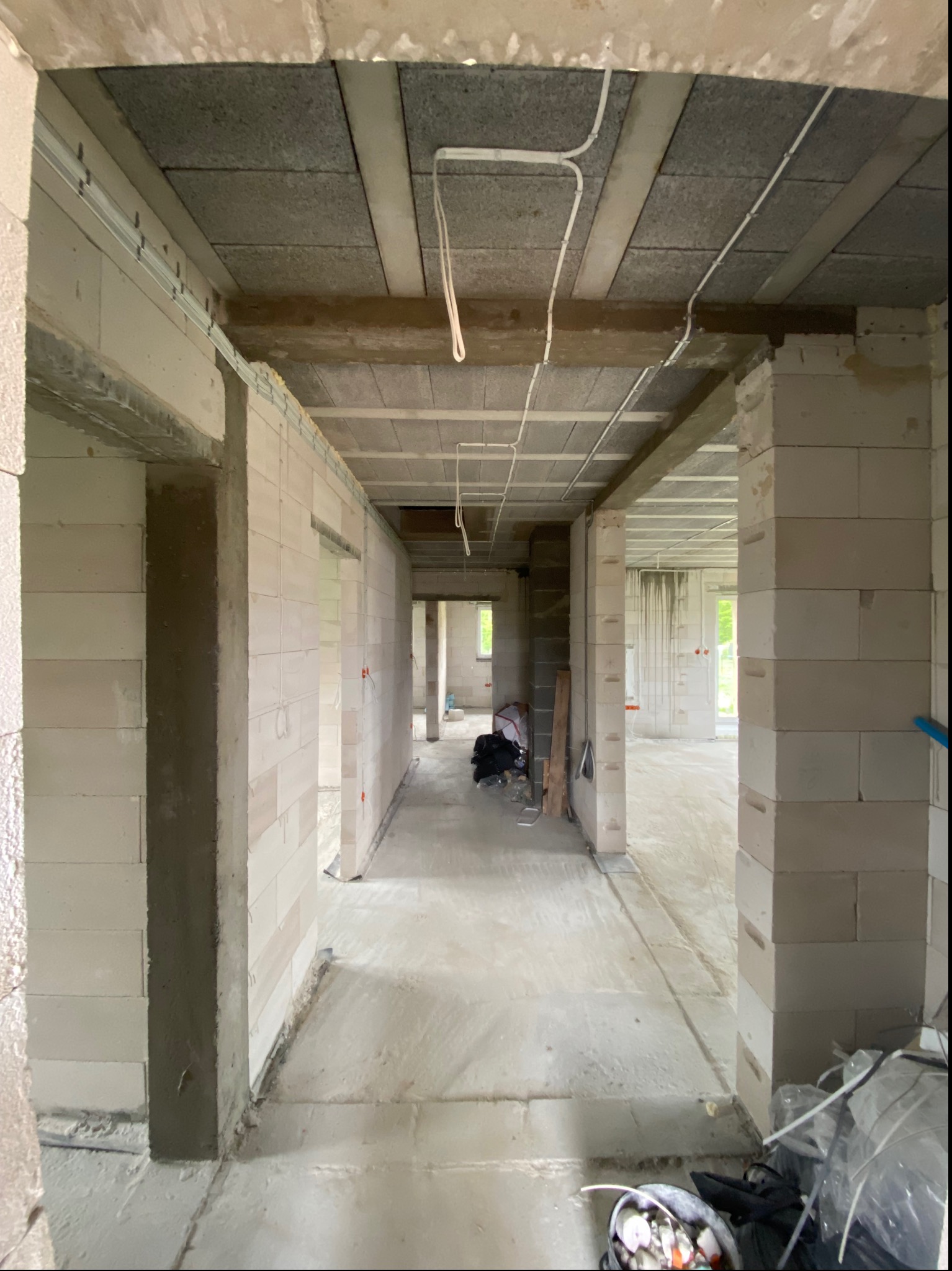 Wnętrze surowego domu w trakcie budowy z widocznymi przewodami elektrycznymi pod sufitem i elementami instalacji elektrycznej w ścianach z betonu komórkowego.