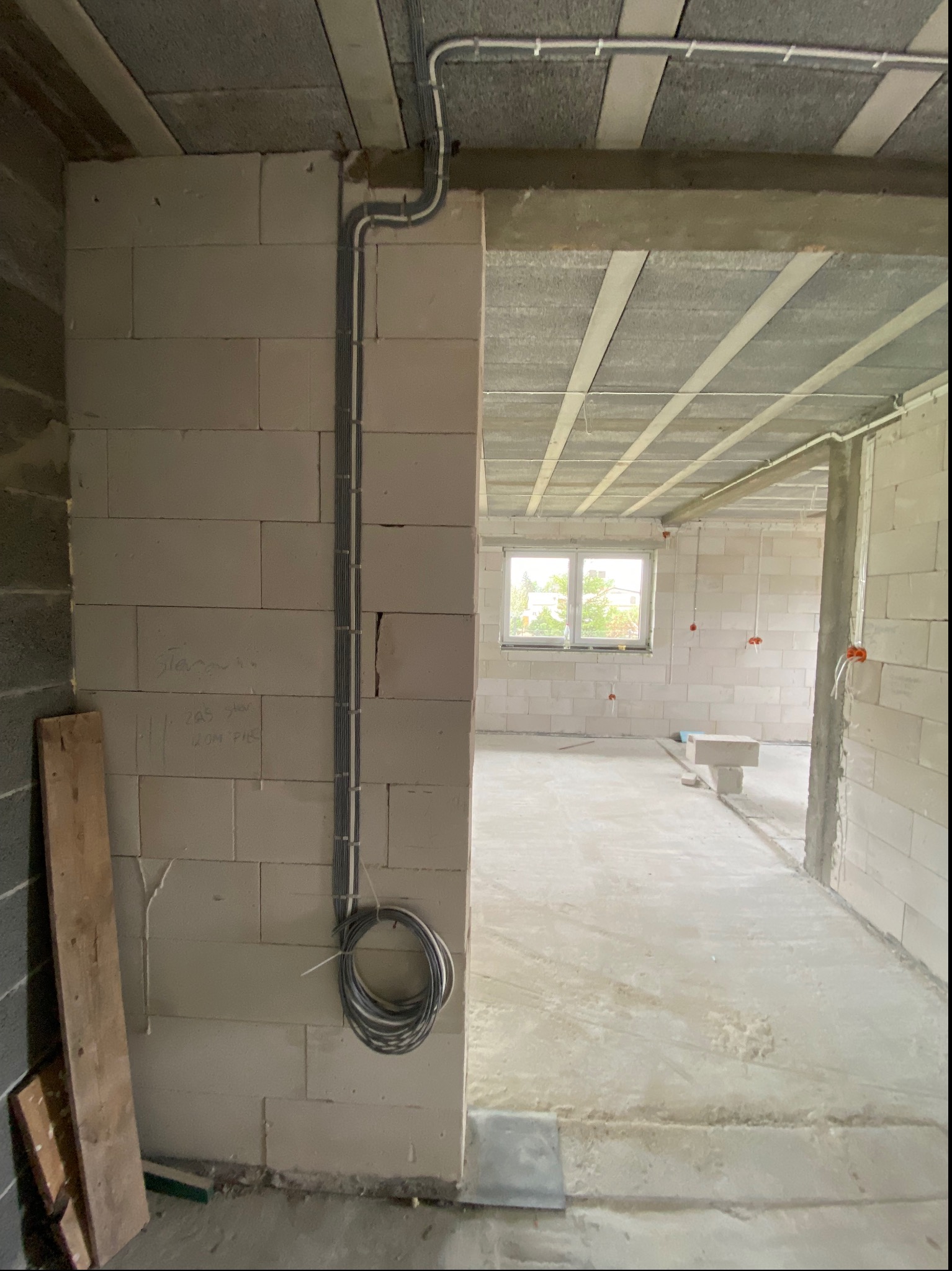 Surowy stan wnętrza budynku w trakcie instalacji elektrycznej: widoczne kable prowadzone po ścianie z betonu komórkowego, zwinięte w pętlę przy podłodze, oraz puszki elektryczne na ścianach w tle.