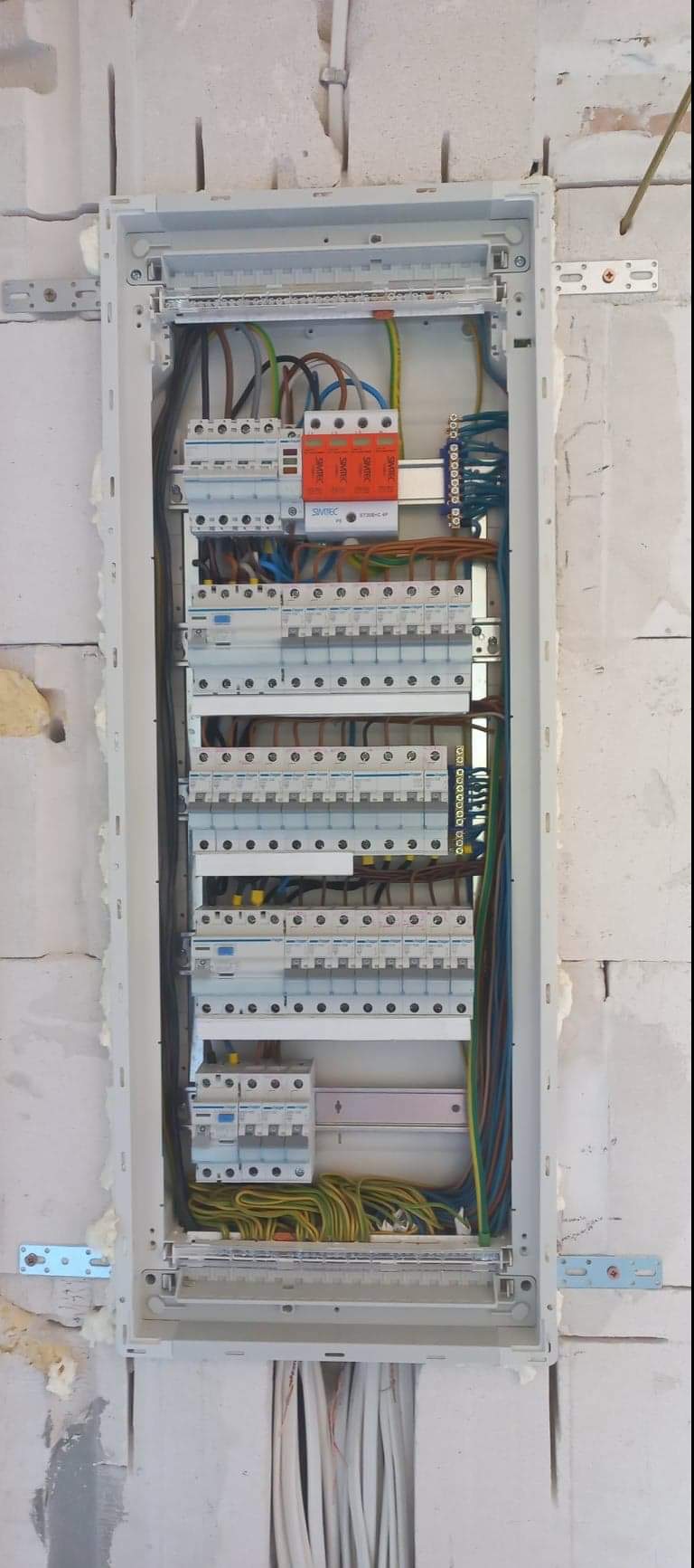 Otwarta skrzynka elektryczna z zainstalowanymi bezpiecznikami, zabezpieczeniami przepięciowymi i przewodami w surowym wnętrzu budynku z bloczków.